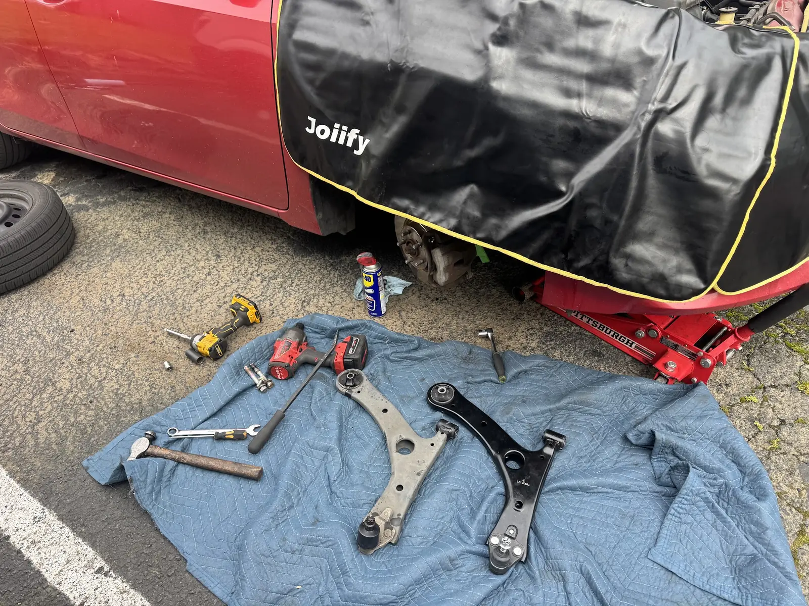 Old and replacement lower control arms beside a 2014 Toyota Corolla during repair.