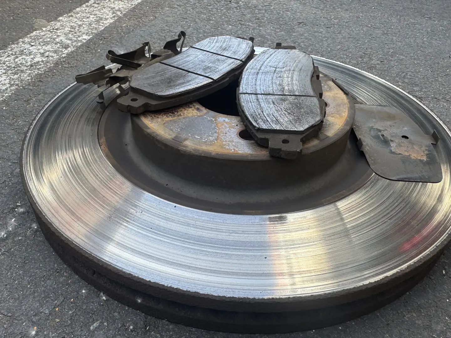 Removed front brake rotor and pads showing uneven wear from a 2014 Nissan Pathfinder.