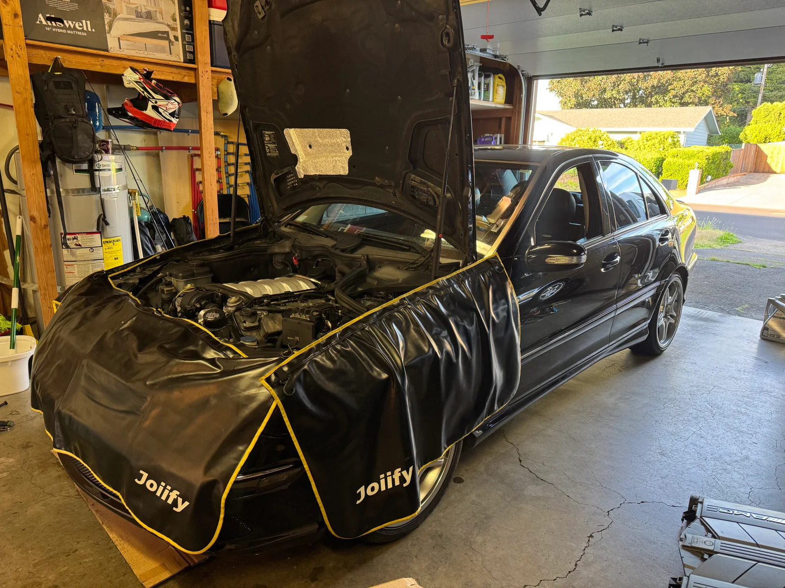 Black Mercedes-Benz C55 AMG with the hood open and protective covers over the front body panels.