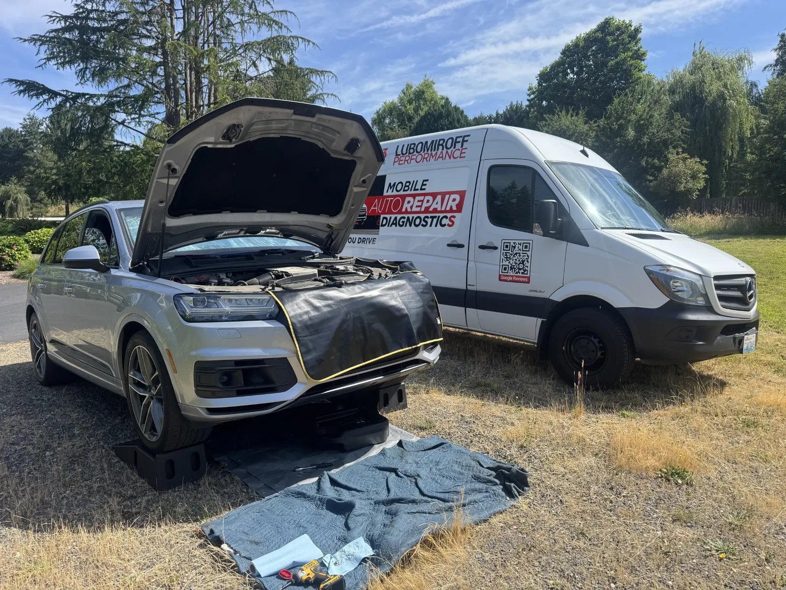 Silver Audi Q7 with its hood open beside the Lubomiroff Performance mobile service van.