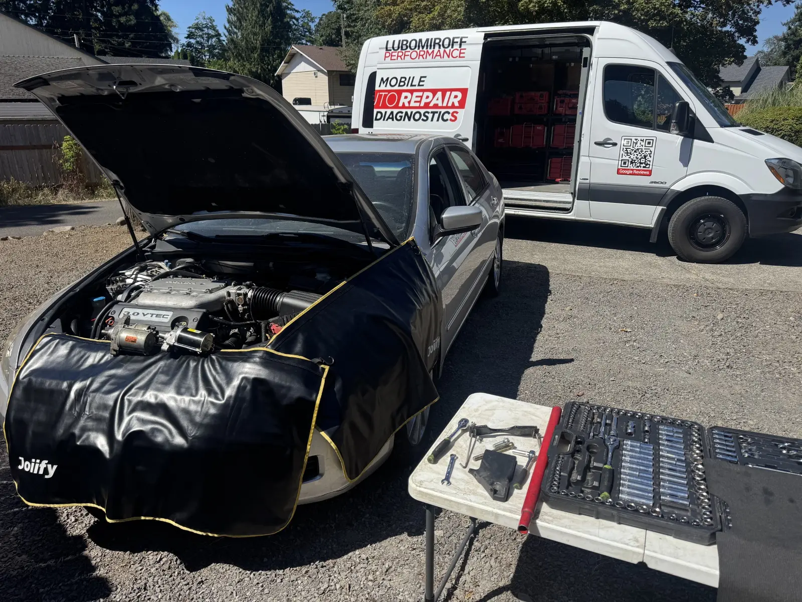 Honda Accord with its hood open, two starters on the fender cover and the Lubomiroff Performance service van behind it.