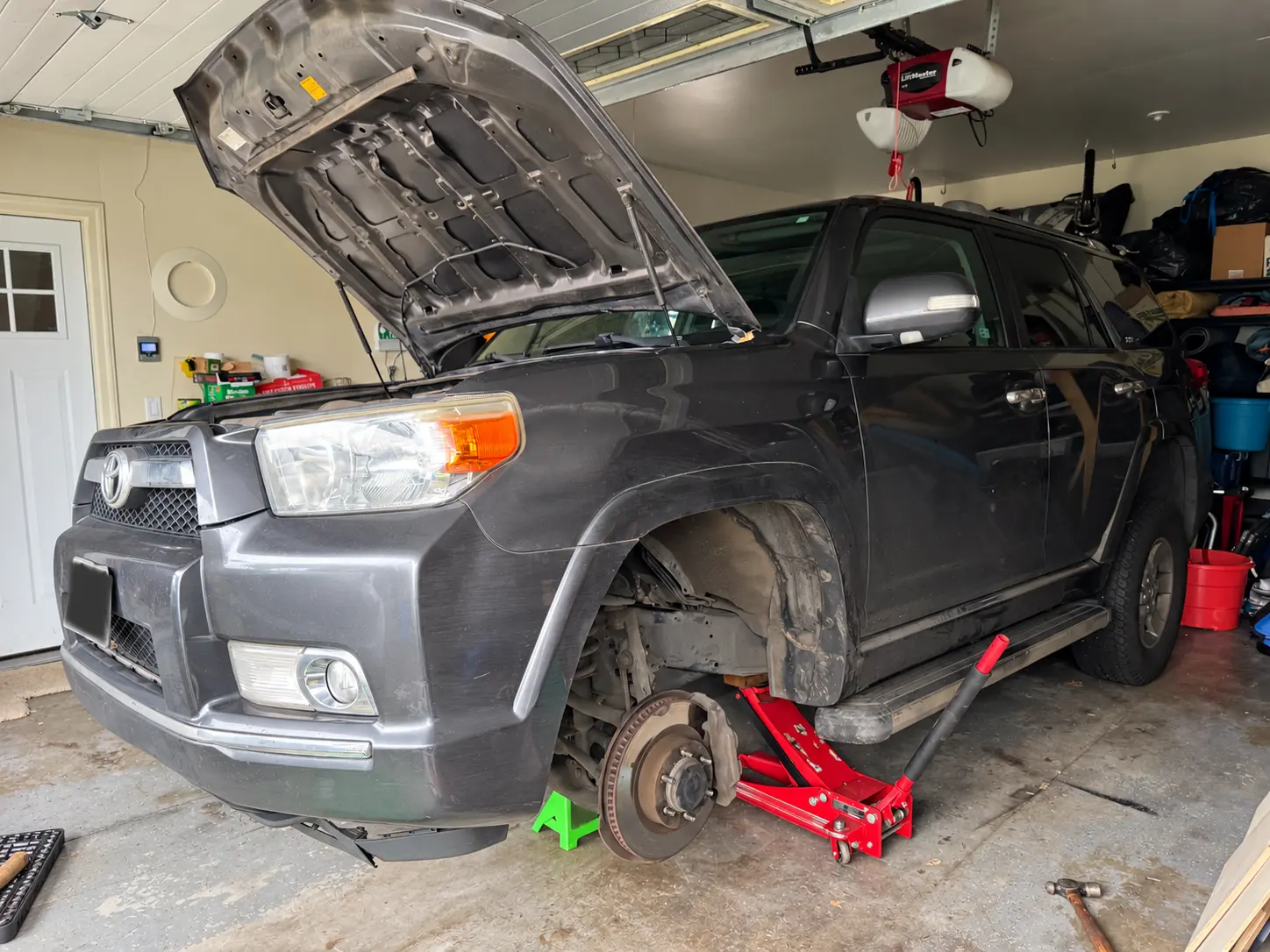 Toyota 4Runner raised on a jack with the hood open and front wheel removed inside a garage.