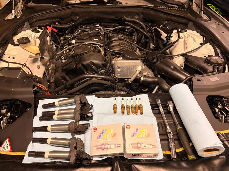 BMW engine bay with ignition coils, spark plugs, and hand tools arranged across the front
