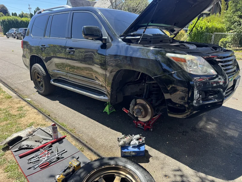 Black Lexus LX 570 raised at the front with a wheel removed and repair tools arranged beside it