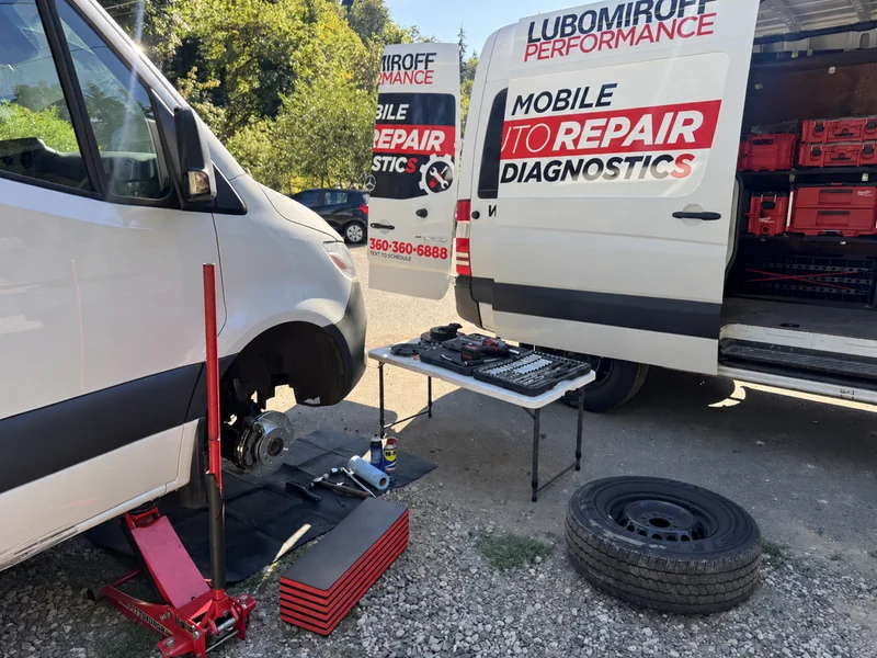 White Mercedes-Benz Sprinter with a front wheel removed beside the Lubomiroff Performance service van and mobile repair tools